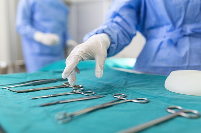 Foto horizontal: Profissional de saúde organiza instrumentos cirúrgicos preparados para procedimento em ambiente hospitalar.
