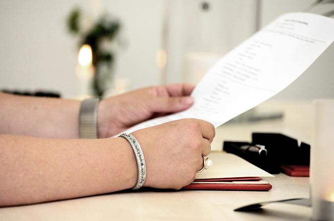 Foto horizontal: Mãos seguram documento sobre mesa, representando análise, conferência ou formalização de ato administrativo.