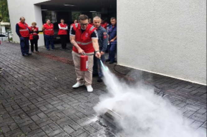 Foto horizontal: participante utiliza extintor durante treinamento prático de combate a incêndio.