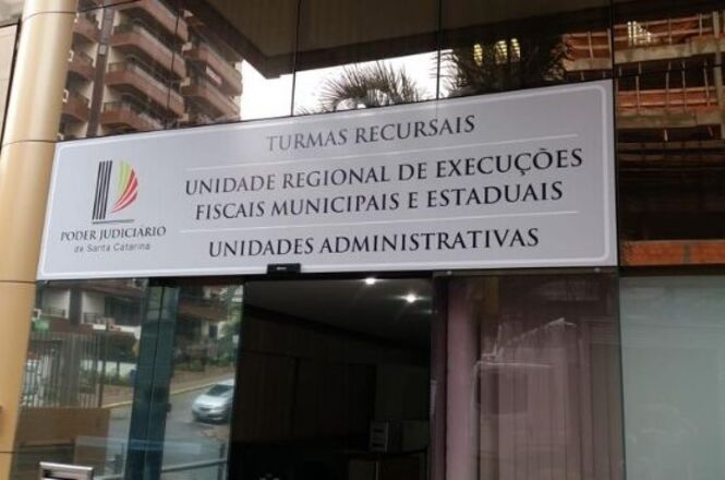 Foto horizontal: placa identifica unidades do Poder Judiciário de Santa Catarina na entrada de edifício.