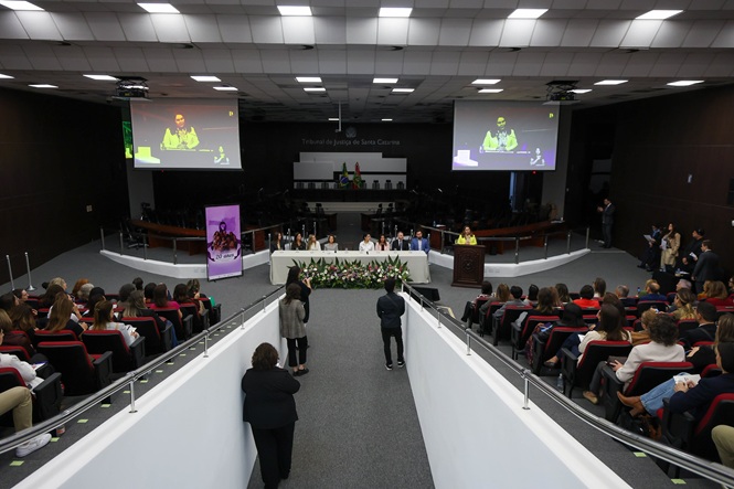 Foto horizontal: público acompanha evento no plenário do TJSC, com autoridades reunidas à mesa principal.