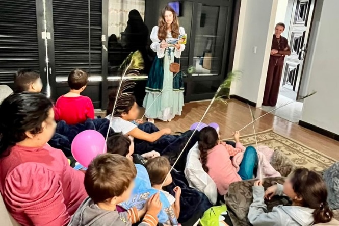 Foto horizontal: crianças acompanham atividade de leitura e contação de histórias em ambiente interno.