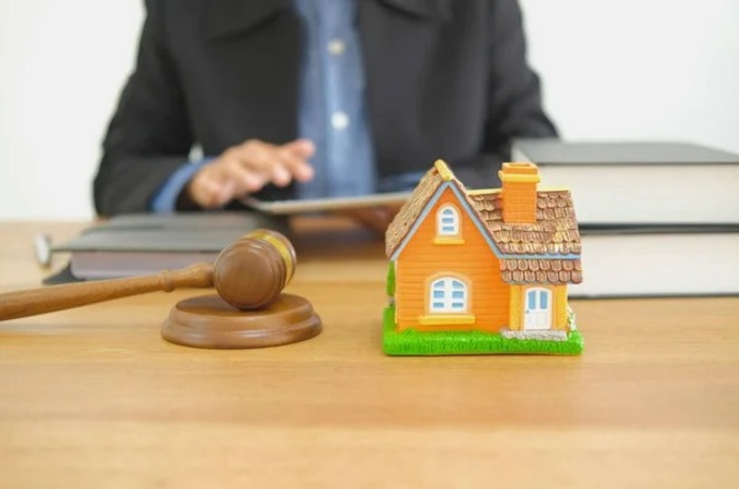 Foto horizontal: miniatura de casa ao lado de martelo judicial, em imagem ilustrativa sobre questões imobiliárias.