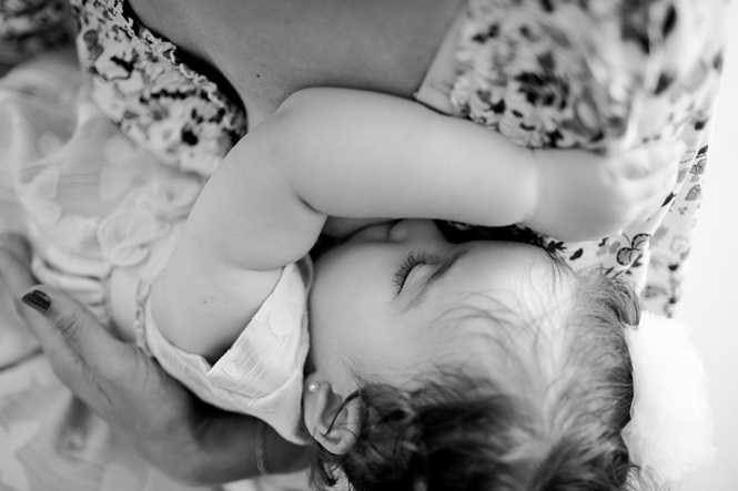 Foto horizontal: bebê é amamentado no colo, em imagem em preto e branco sobre aleitamento materno.