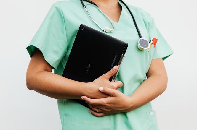 Foto horizontal: profissional da saúde segura tablet e usa estetoscópio, em imagem ilustrativa.