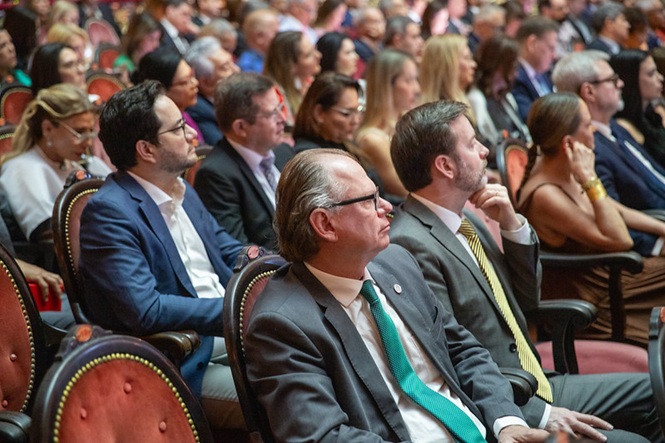 Foto horizontal: desembargador Rubens Schulz, de gravata verde, acompanha evento sentado na plateia.