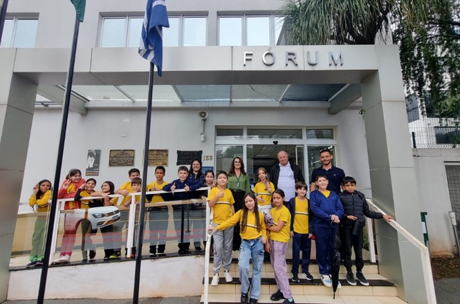 Imagem horizontal mostra estudantes e adultos reunidos em frente à entrada de um fórum.