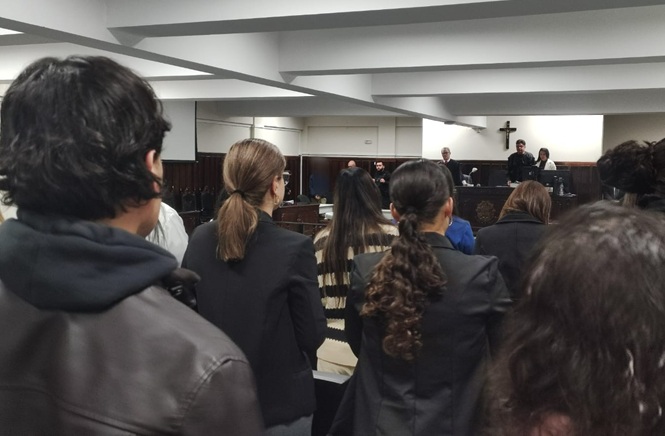 Imagem horizontal mostra público em pé acompanhando sessão em plenário, com autoridades à frente.
