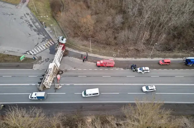 Imagem horizontal aérea mostra caminhão tombado em rodovia, com veículos de emergência no local.