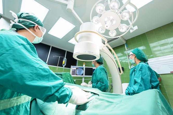 Imagem horizontal mostra equipe médica realizando procedimento cirúrgico em sala equipada com aparelhos hospitalares.