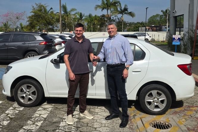 Foto horizontal: dois homens posam ao lado de um carro branco, enquanto um deles segura a chave do veículo.