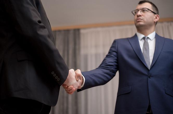 Foto horizontal: dois homens de terno apertam as mãos em gesto de cumprimento ou acordo.