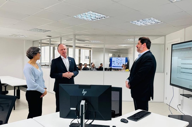Foto horizontal: desembargador Rubens Schulz conversa com dois servidores durante visita a ambiente de trabalho com equipamentos de informática.