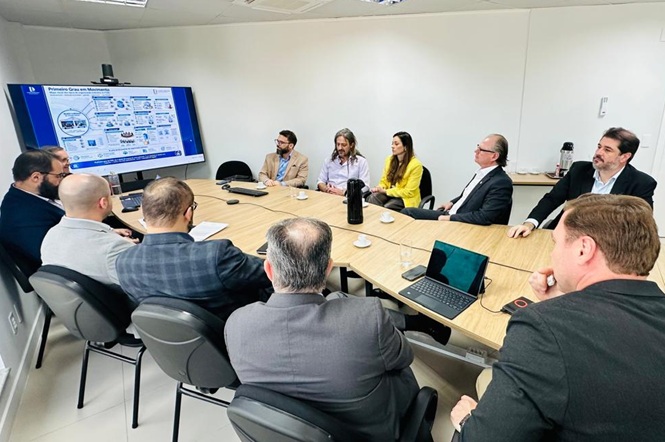 Foto horizontal: desembargador Rubens Schulz, ao lado de mulher de blazer amarelo, participa de reunião com apresentação exibida em tela.