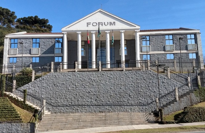 Foto horizontal: fachada do prédio do Fórum, com ampla escadaria de acesso, colunas e bandeiras em frente à entrada principal.