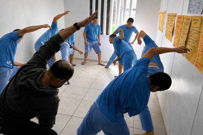 Foto horizontal: grupo de adolescentes em cumprimento de medida socioeducativa realiza exercícios de alongamento durante atividade coletiva.