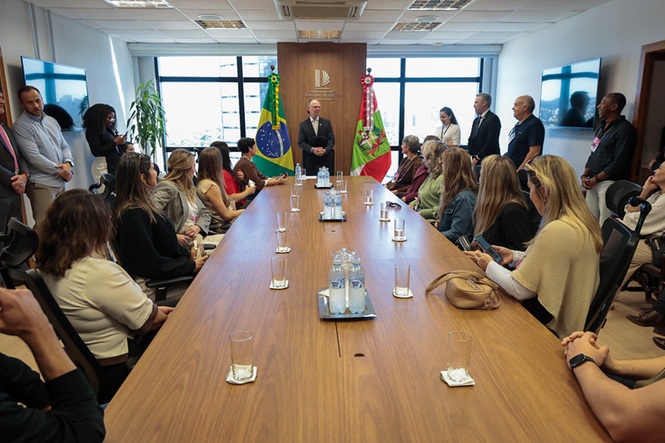 Foto horizontal: presidente do TJSC, Rubens Schulz, fala diante de grupo reunido em sala, entre as bandeiras do Brasil e de Santa Catarina.
