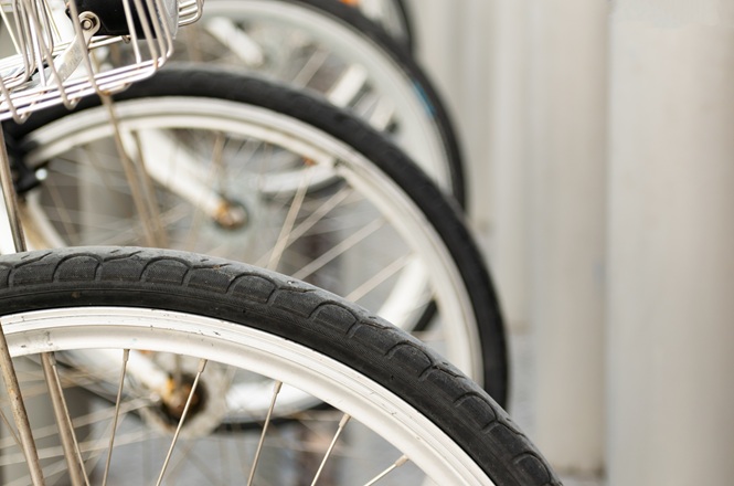Foto horizontal: detalhe das rodas de bicicletas posicionadas lado a lado, com pneus, aros e raios em destaque.