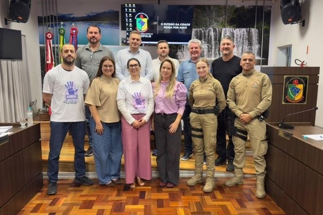 Foto horizontal: grupo de homens e mulheres, incluindo policiais militares, posa para registro coletivo em plenário, durante encontro institucional.
