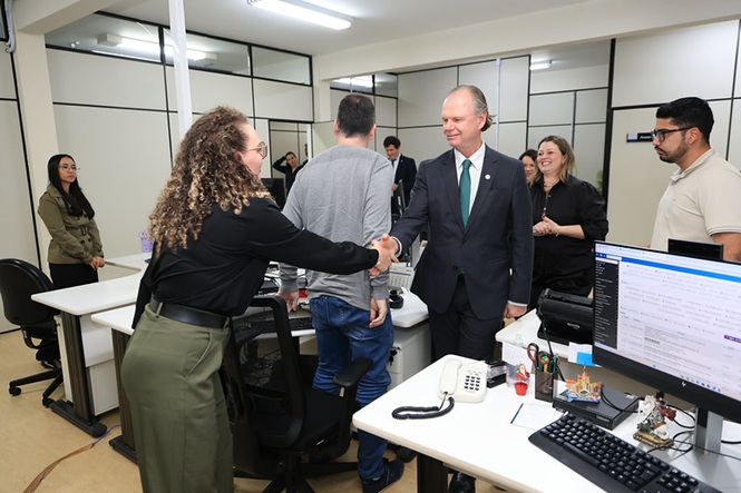 Foto horizontal: presidente do TJSC, desembargador Rubens Schulz, cumprimenta servidora com aperto de mãos durante visita a setor de trabalho.