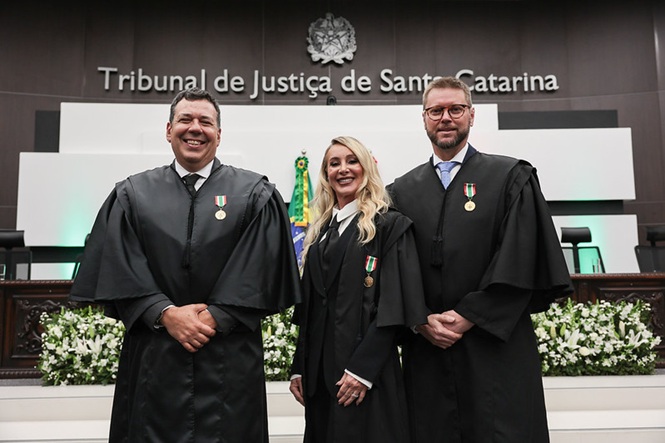 Foto horizontal: desembargadores Cláudio Eduardo Regis de Figueiredo e Silva, Margani de Mello e Giancarlo Bremer Nones posam sorridentes, de toga e com medalhas, no Tribunal de Justiça de Santa Catarina.