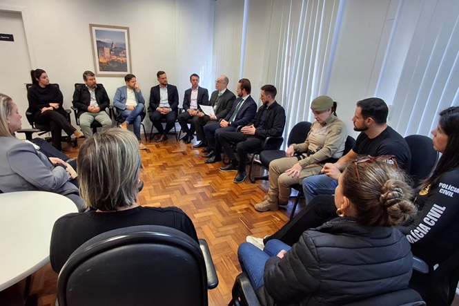 Foto horizontal: representantes do Judiciário, forças de segurança e instituições parceiras participam de reunião em sala, sentados em círculo.