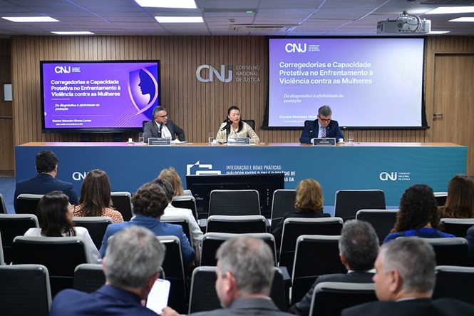Foto horizontal: três integrantes compõem mesa de apresentação no CNJ, diante do público, durante debate sobre o enfrentamento à violência contra as mulheres.