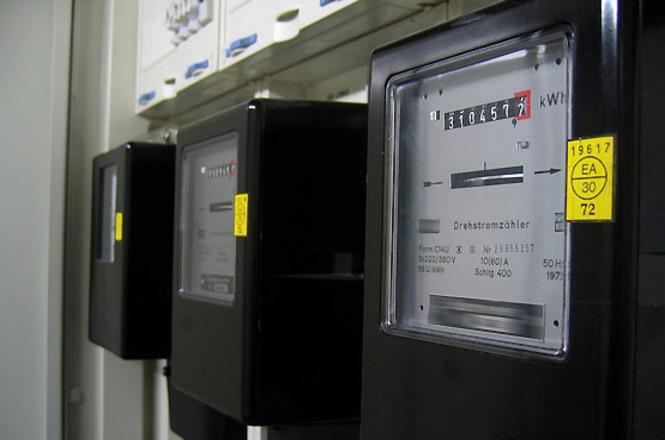 Foto horizontal: medidores de energia elétrica aparecem instalados lado a lado em painel interno.