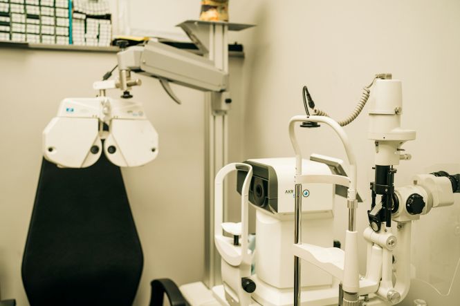 Foto horizontal: equipamentos utilizados para exames oftalmológicos aparecem em consultório, com cadeira de atendimento ao fundo.