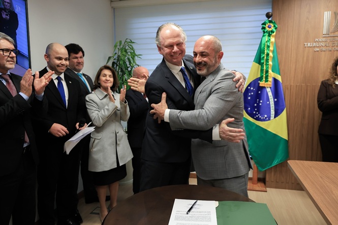 Foto horizontal: des. Rubens Schulz abraça o presidente interino do TJSC, des. André Luiz Dacol, enquanto autoridades aplaudem.