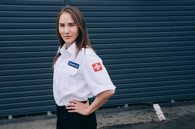 Foto horizontal: mulher uniformizada posa para foto, com símbolo da cruz vermelha na manga da camisa branca.