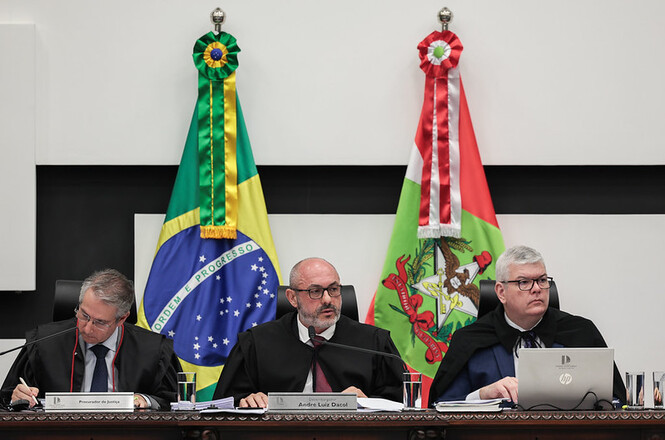 Foto horizontal: presidente do TJSC, des. André Luiz Dacol, ao centro, durante sessão, com magistrados e bandeiras do Brasil e de Santa Catarina ao fundo.