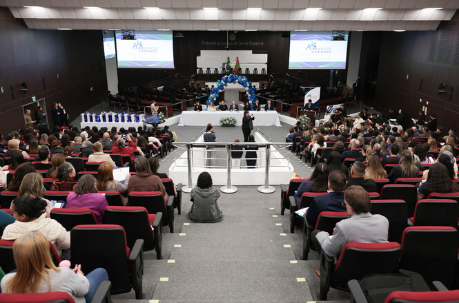 Foto horizontal: público lota o plenário do TJSC durante evento do programa Novos Caminhos, com palco e decoração ao centro.