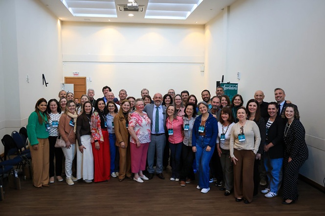 Foto horizontal: grupo de servidores e participantes posa para foto em auditório, ao final de atividade institucional.