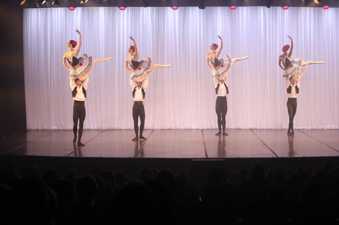 Foto horizontal: bailarinos executam coreografia de balé no palco, diante do público durante apresentação artística.
