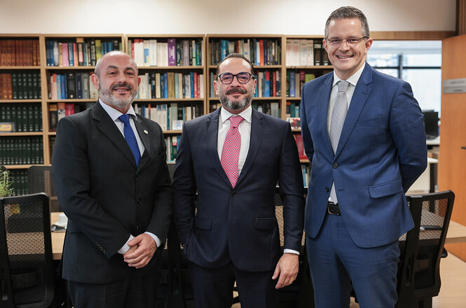 Foto horizontal: presidente em exercício do TJSC, des. André Luiz Dacol, de gravata azul, posa ao lado de duas autoridades.