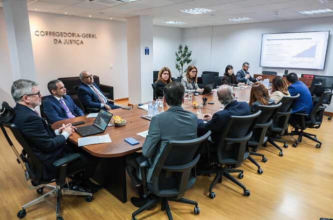 Foto horizontal: autoridades participam de reunião na Corregedoria-Geral da Justiça, com apresentação exibida em tela.