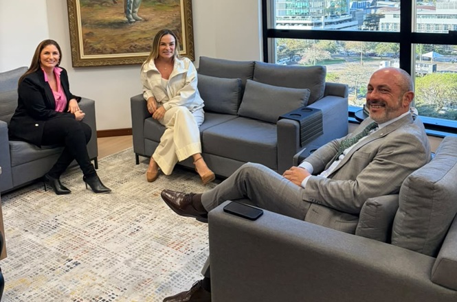 Foto horizontal: magistradas Érica Lourenço e Ana Blasi posam sentadas com o desembargador André Dacol, em sala de tons cinza.