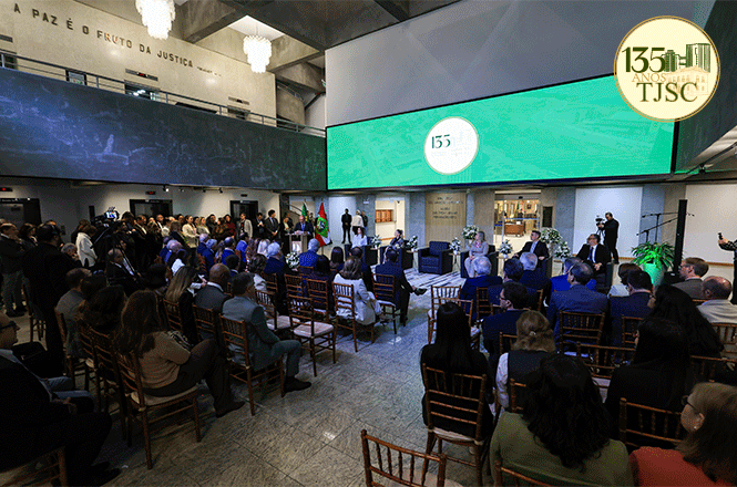 Foto horizontal: público acompanha solenidade dos 135 anos do TJSC em hall decorado com painéis verdes e iluminação azul.