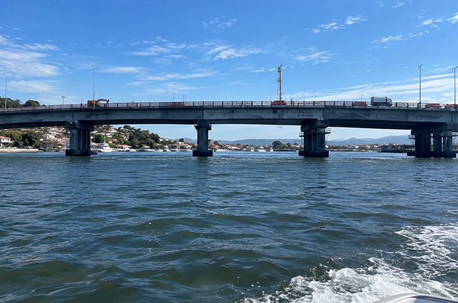 Foto horizontal: vista da Ponte Colombo Salles sobre o mar, com veículos circulando sob céu azul em Florianópolis.