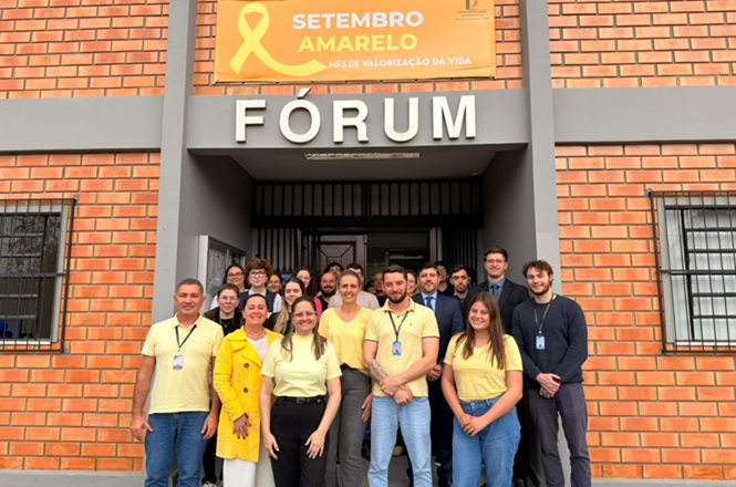 Foto horizontal: servidores posam em frente ao Fórum, vestidos de amarelo em apoio à campanha Setembro Amarelo de valorização da vida.