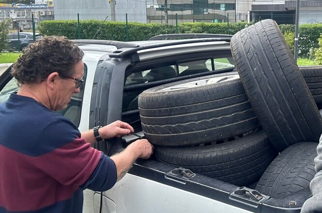 Foto horizontal: homem organiza pneus usados na carroceria de uma caminhonete, estacionada em área urbana.