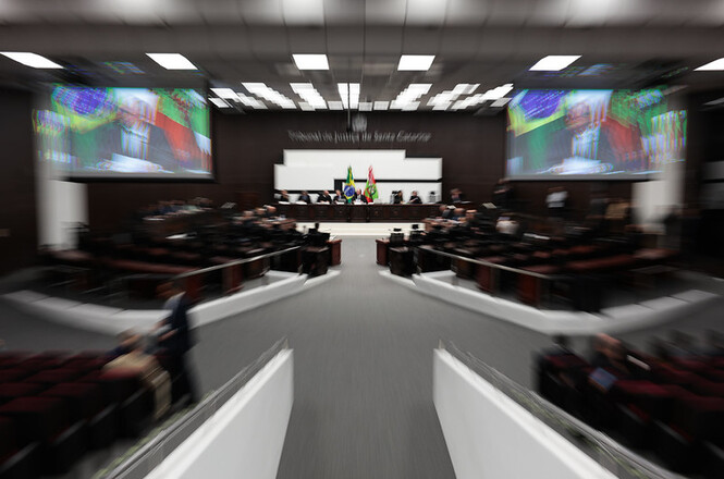 Foto colorida: plenário do Tribunal de Justiça com autoridades e público, ambiente institucional amplo, sessão judicial, acompanhando julgamentos em preto, branco e vermelho