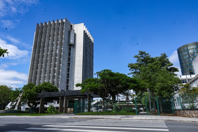 Foto colorida: prédio do Poder Judiciário de Santa Catarina, área urbana arborizada, sede institucional, destacando fachada em cinza, verde e azul.