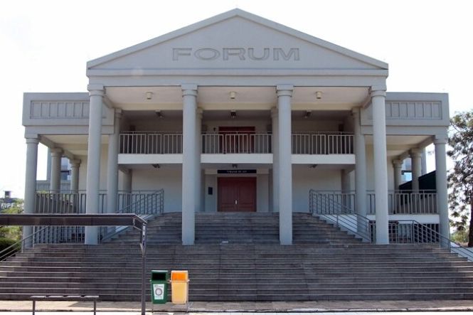 Foto horizontal: prédio do fórum cinza com colunas sob céu claro exibe fachada imponente com ampla escadaria.