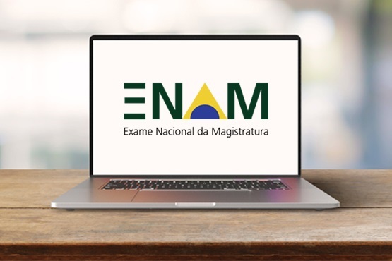 Notebook aberto em cima de mesa de madeira com imagem escrito "ENAM - Exame Nacional da Magistratura" na tela